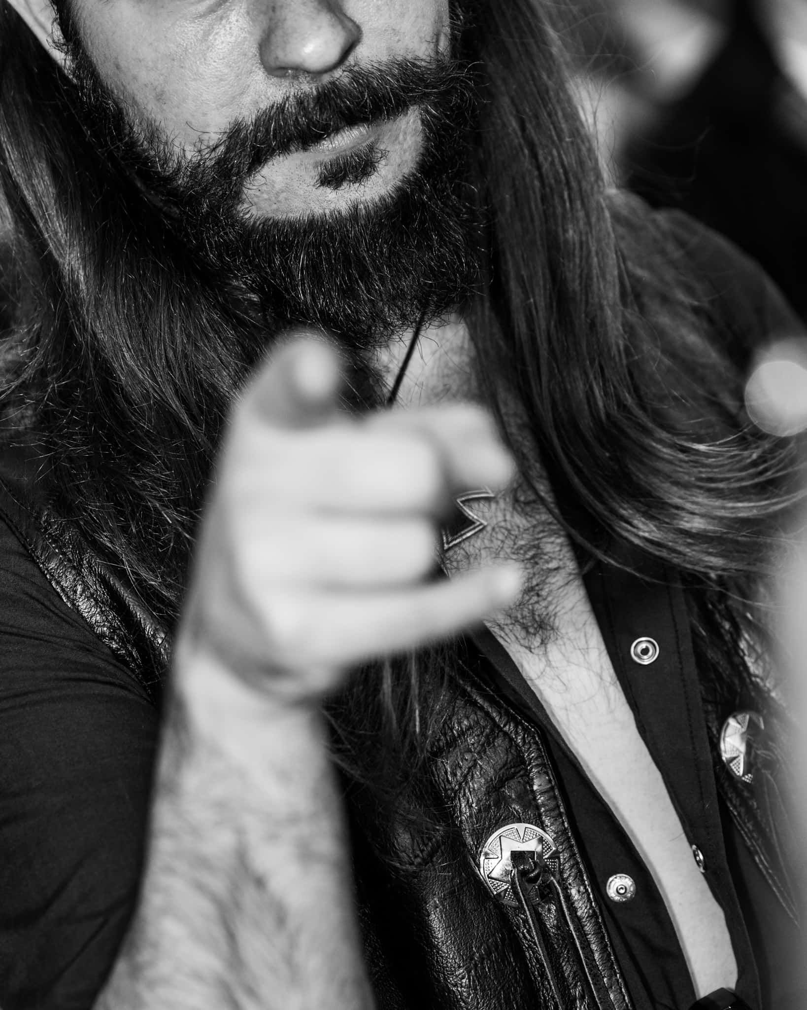 A man with long hair and a beard is pointing at the camera