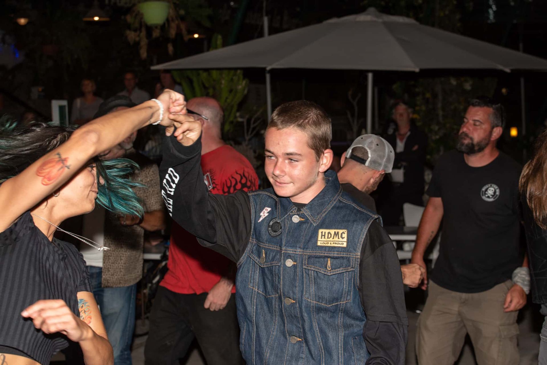 A man in a denim vest is dancing in a crowd of people.