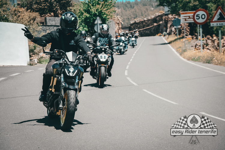 A group of people riding motorcycles down a road with a 50 sign in the background