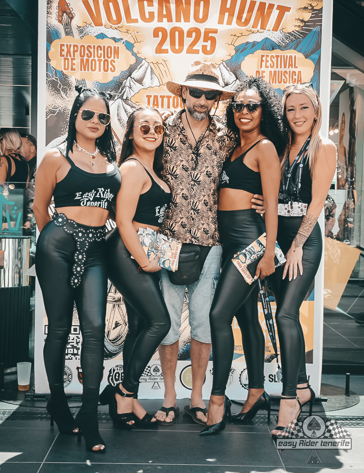 Five people pose for a photo in front of a festival banner, four women in black outfits with a man in the center.