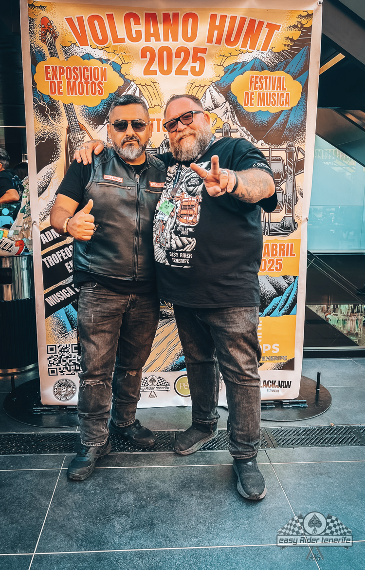 Two men pose in front of a banner 