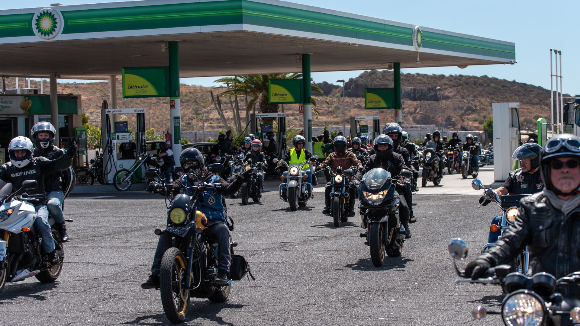 A group of people are riding motorcycles in front of a gas station.