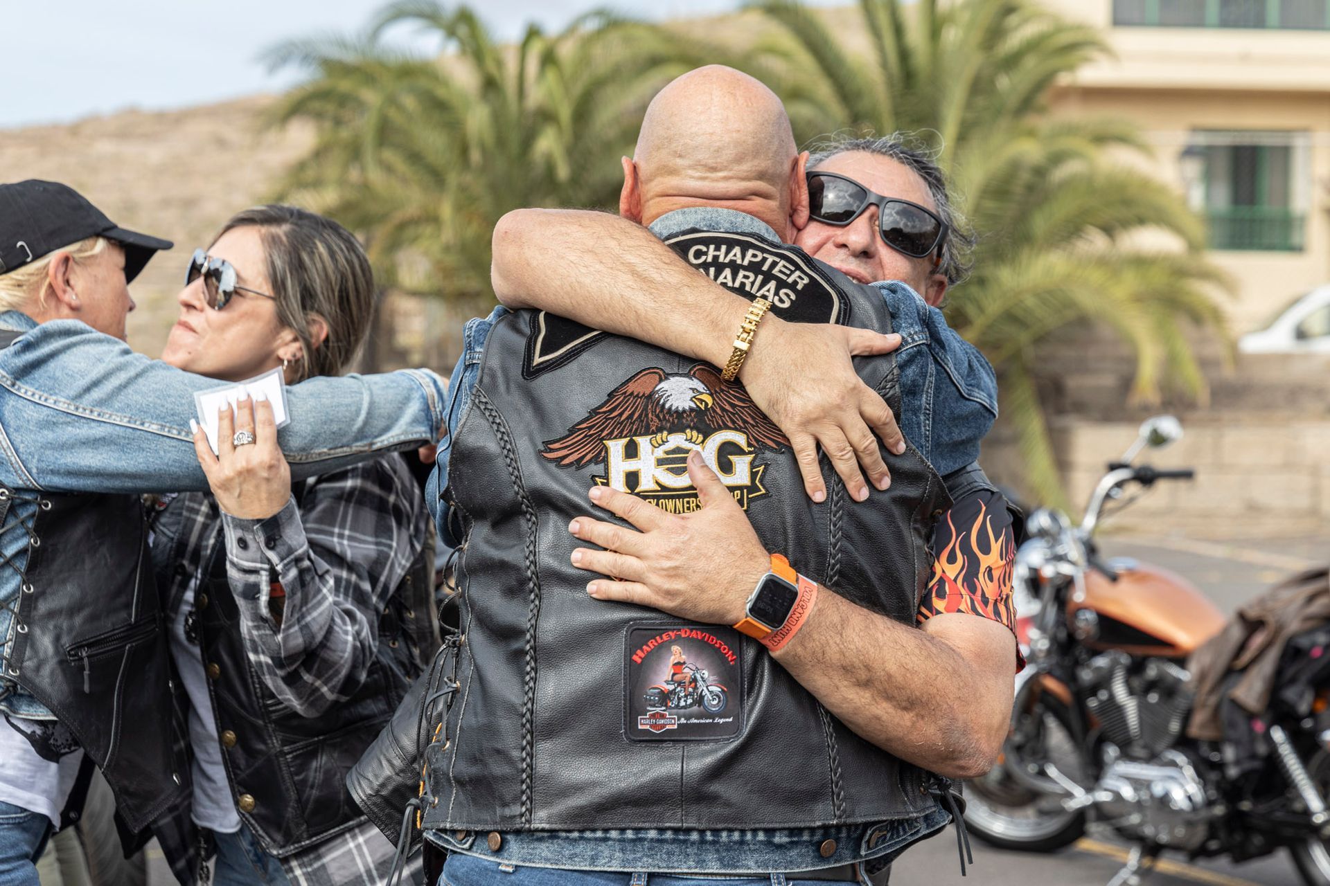 A group of people are hugging each other in front of motorcycles.