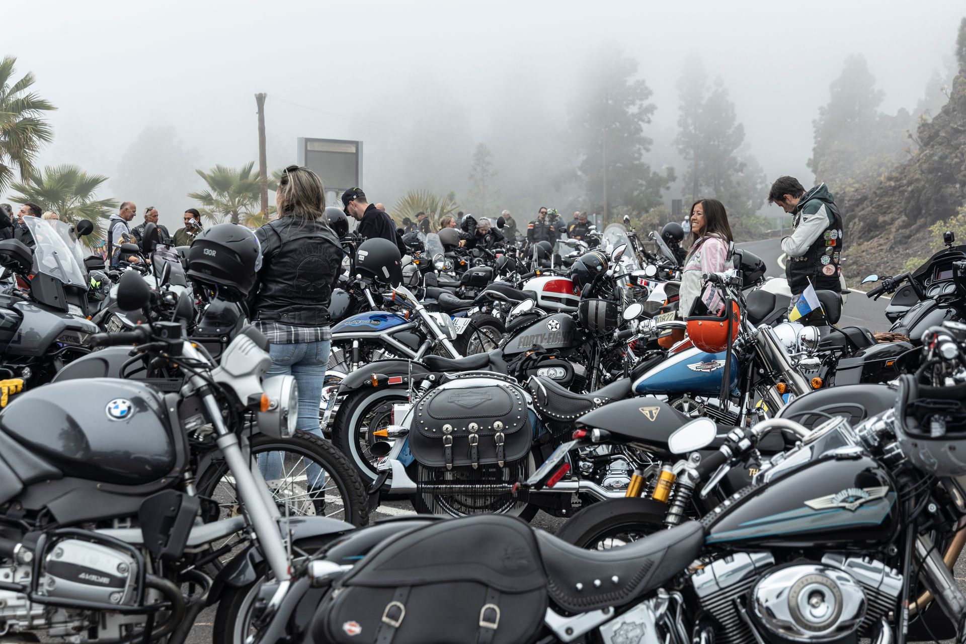 A lot of motorcycles are parked in a parking lot on a foggy day.