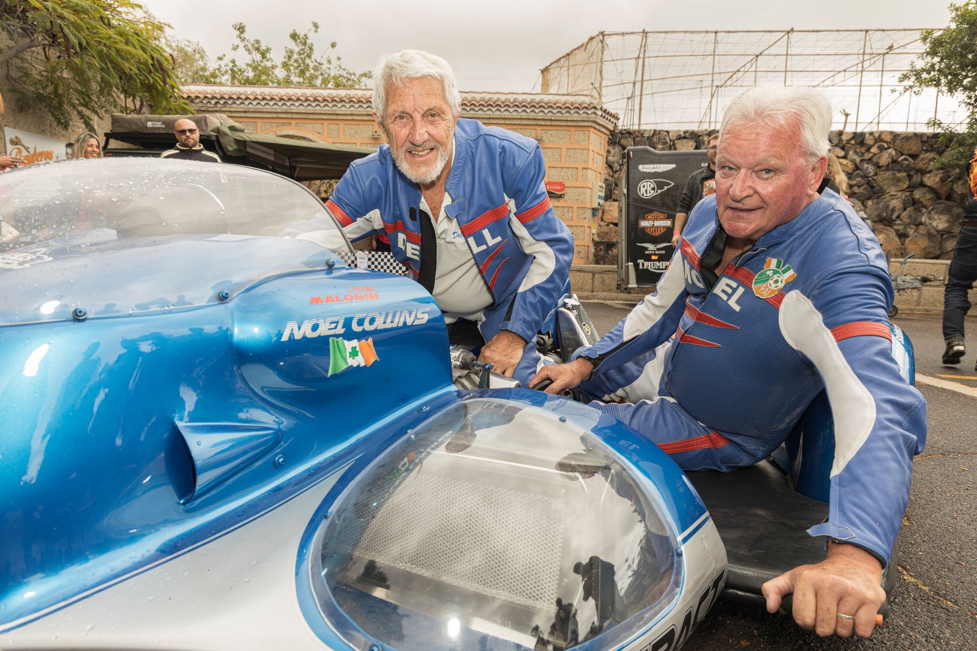 Two men are sitting next to a blue and white race car.