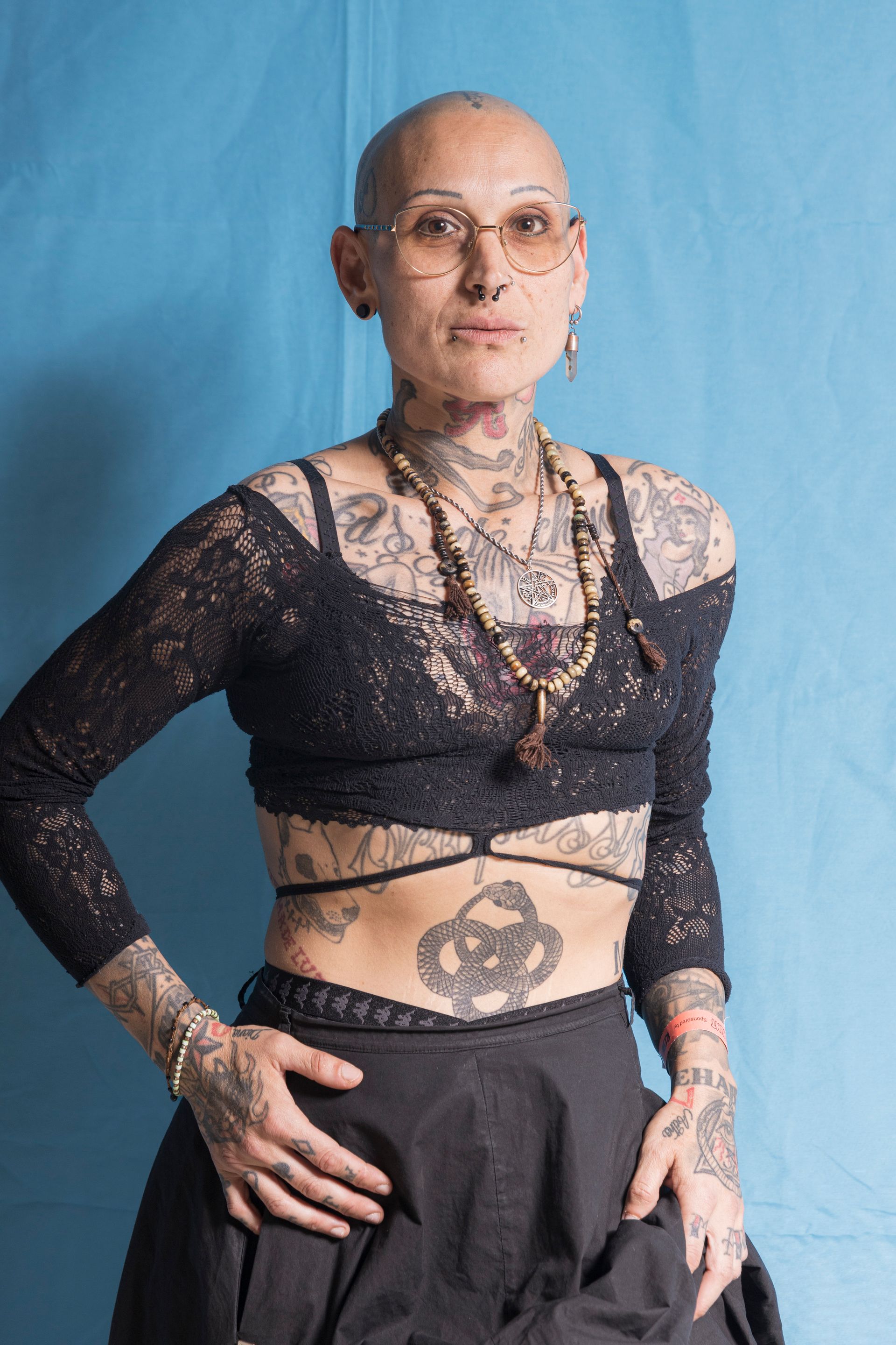 A woman with a lot of tattoos on her body is standing in front of a blue wall.