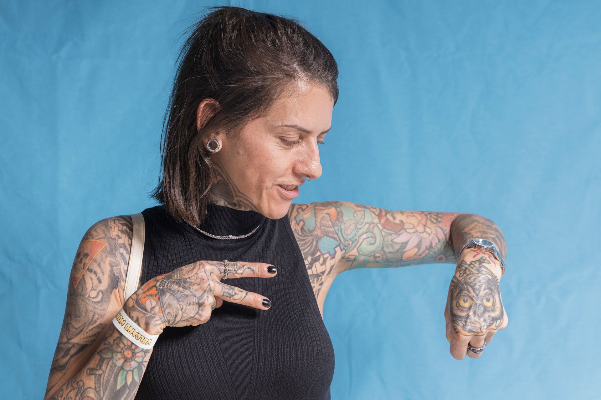 A woman with a lot of tattoos on her arms is pointing at her watch.