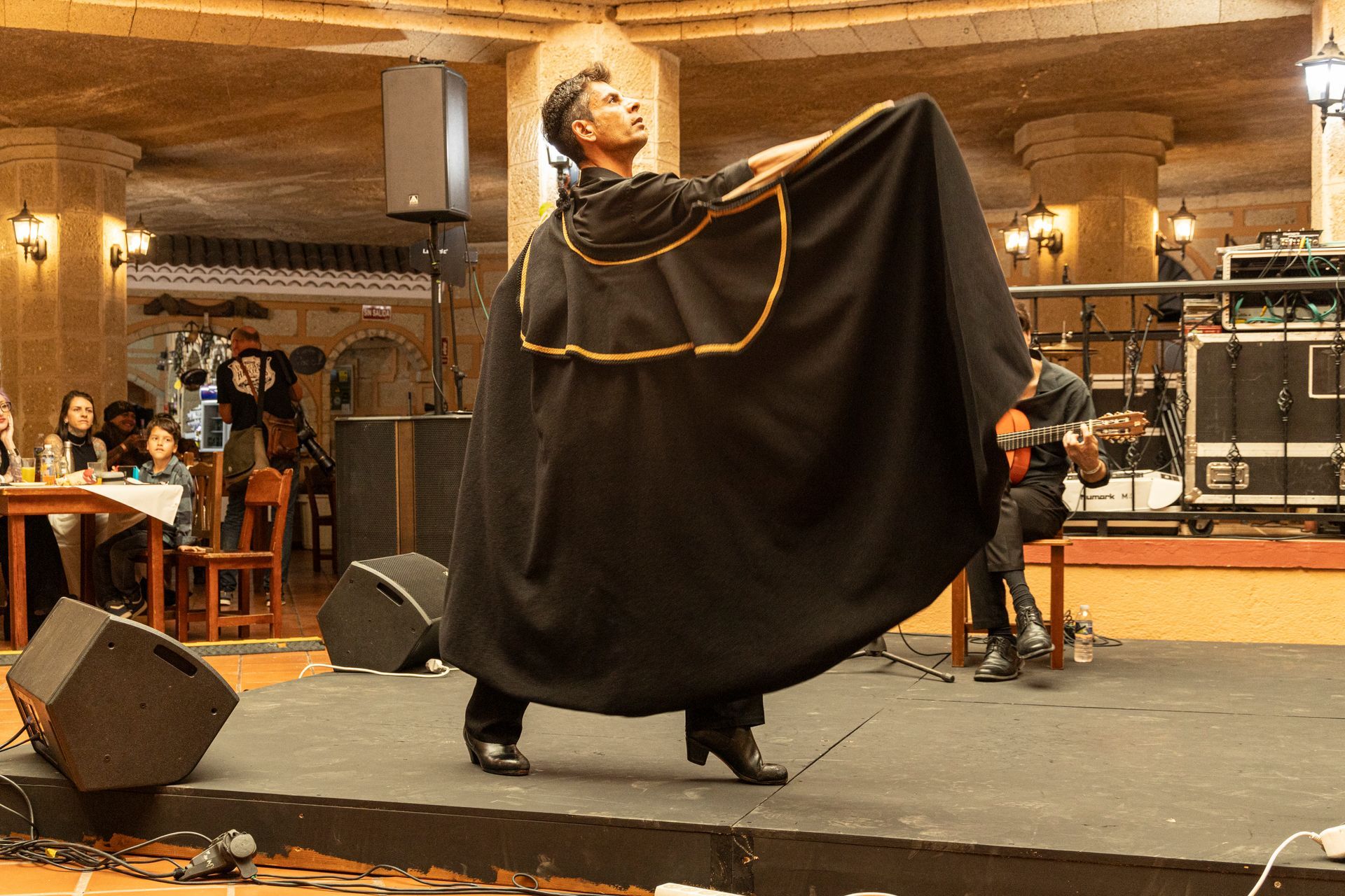 A man in a black cape is dancing on a stage