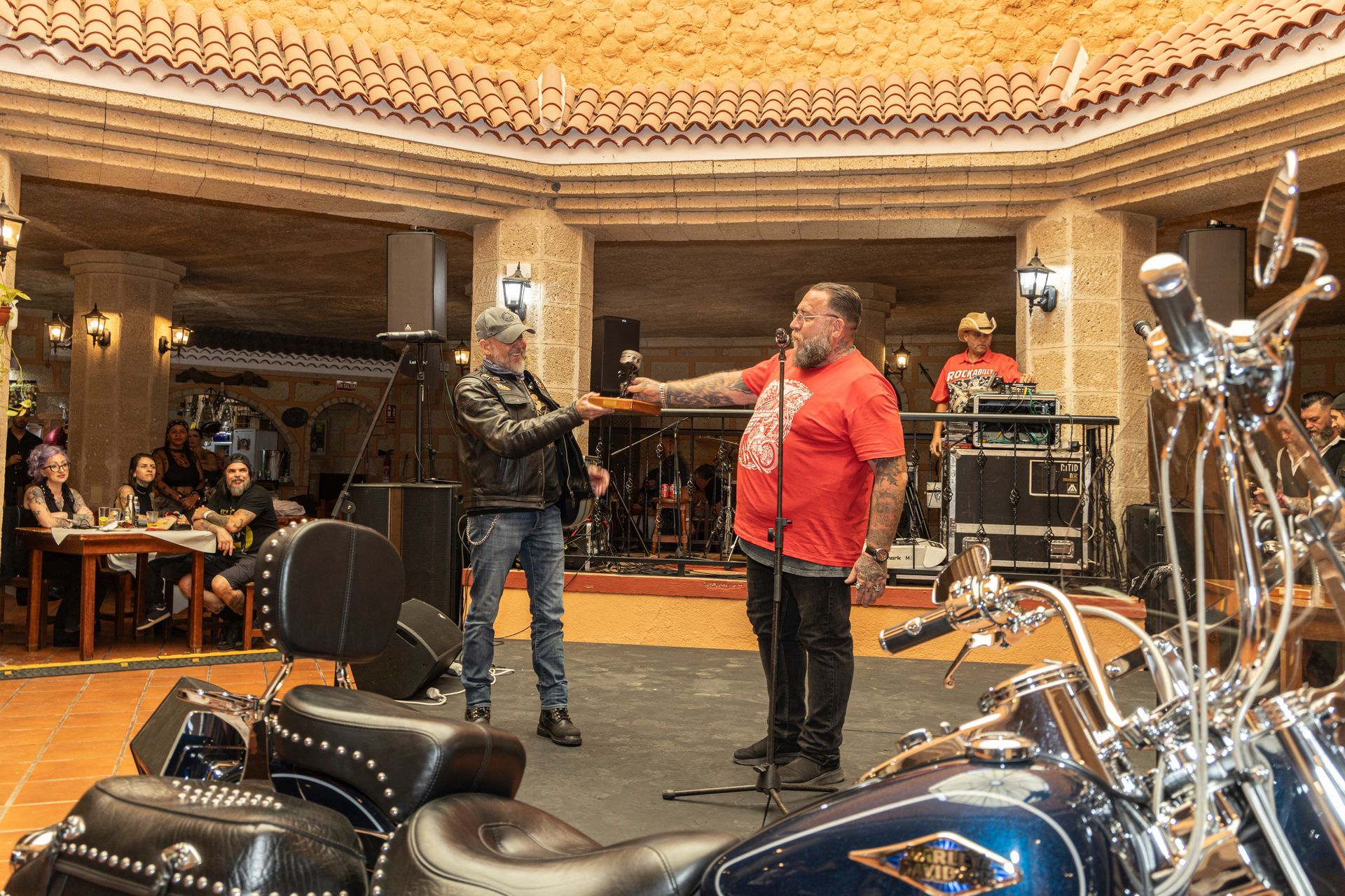 Two men are standing in front of a microphone in a room with motorcycles.
