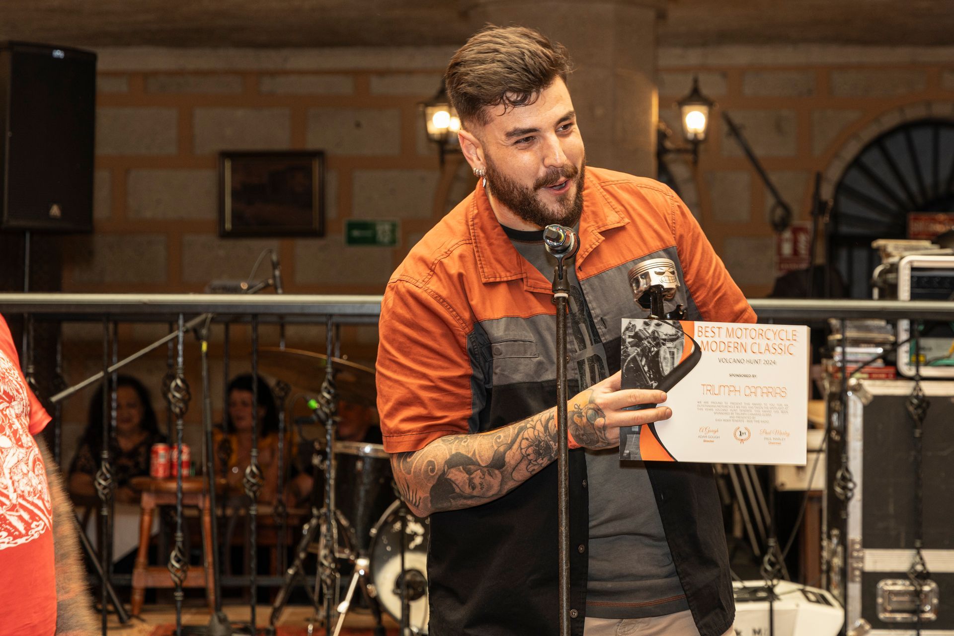 A man with a beard is standing in front of a microphone holding a piece of paper.
