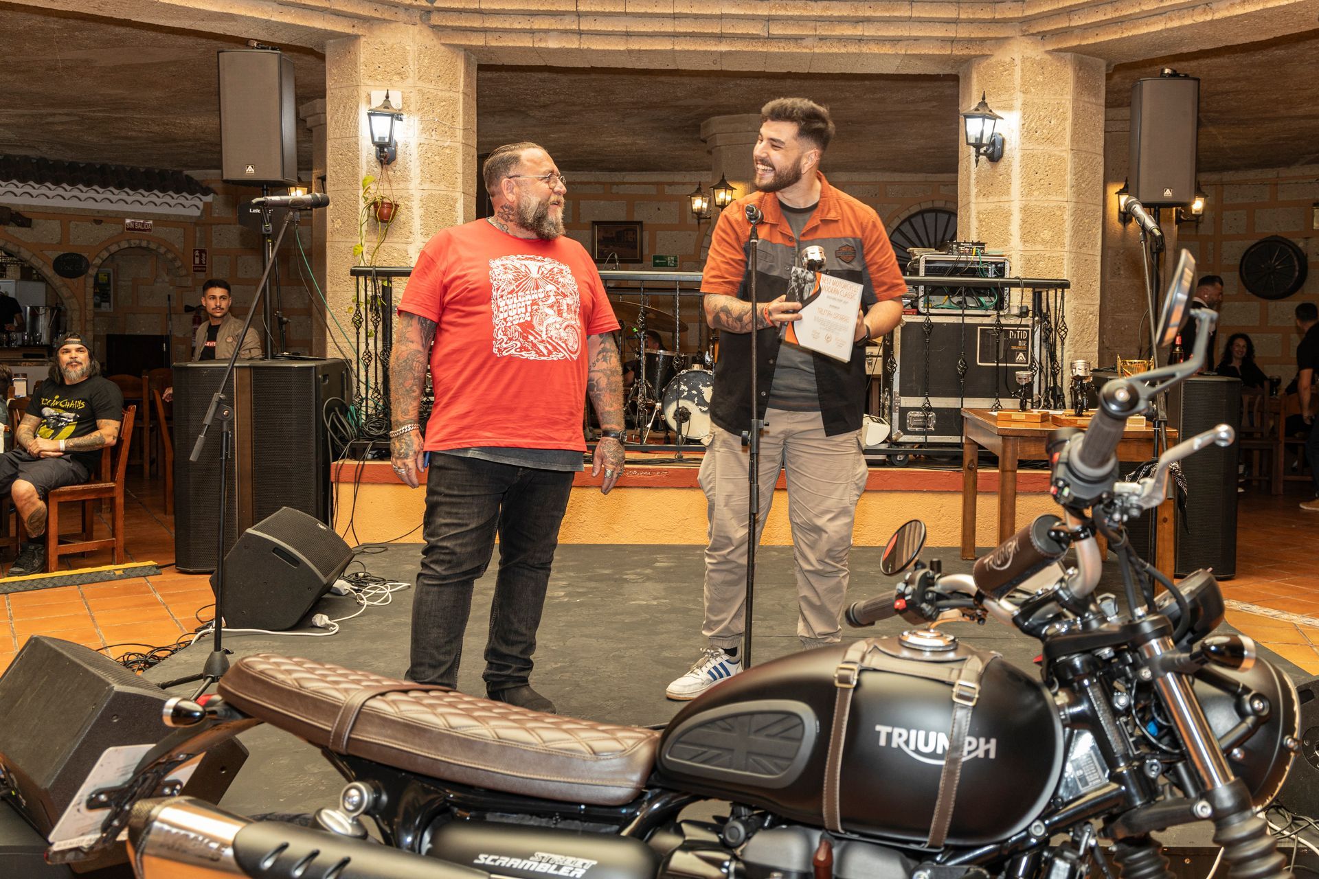 Two men are standing next to a motorcycle in a room.