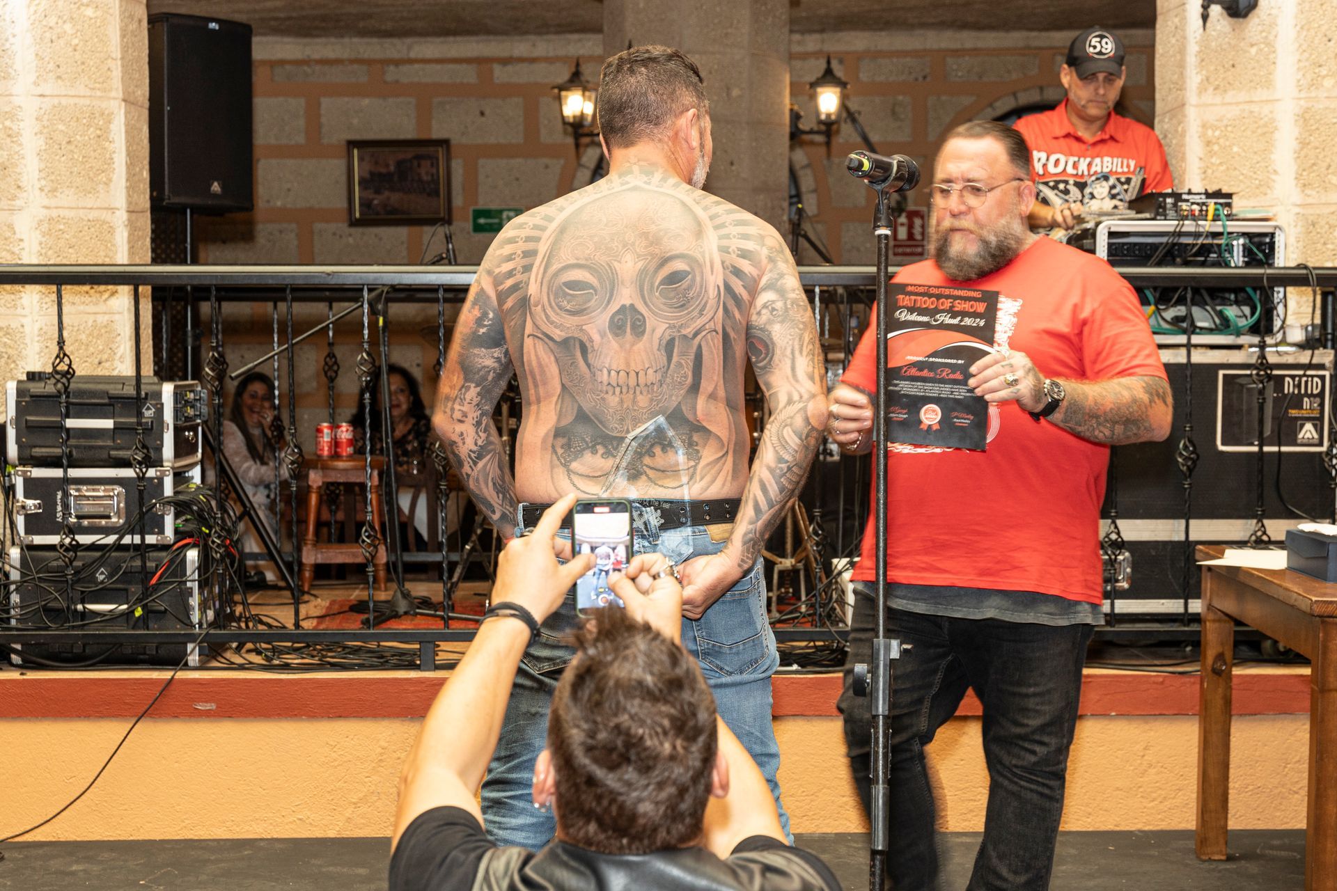A man with a tattoo on his back is standing next to another man.