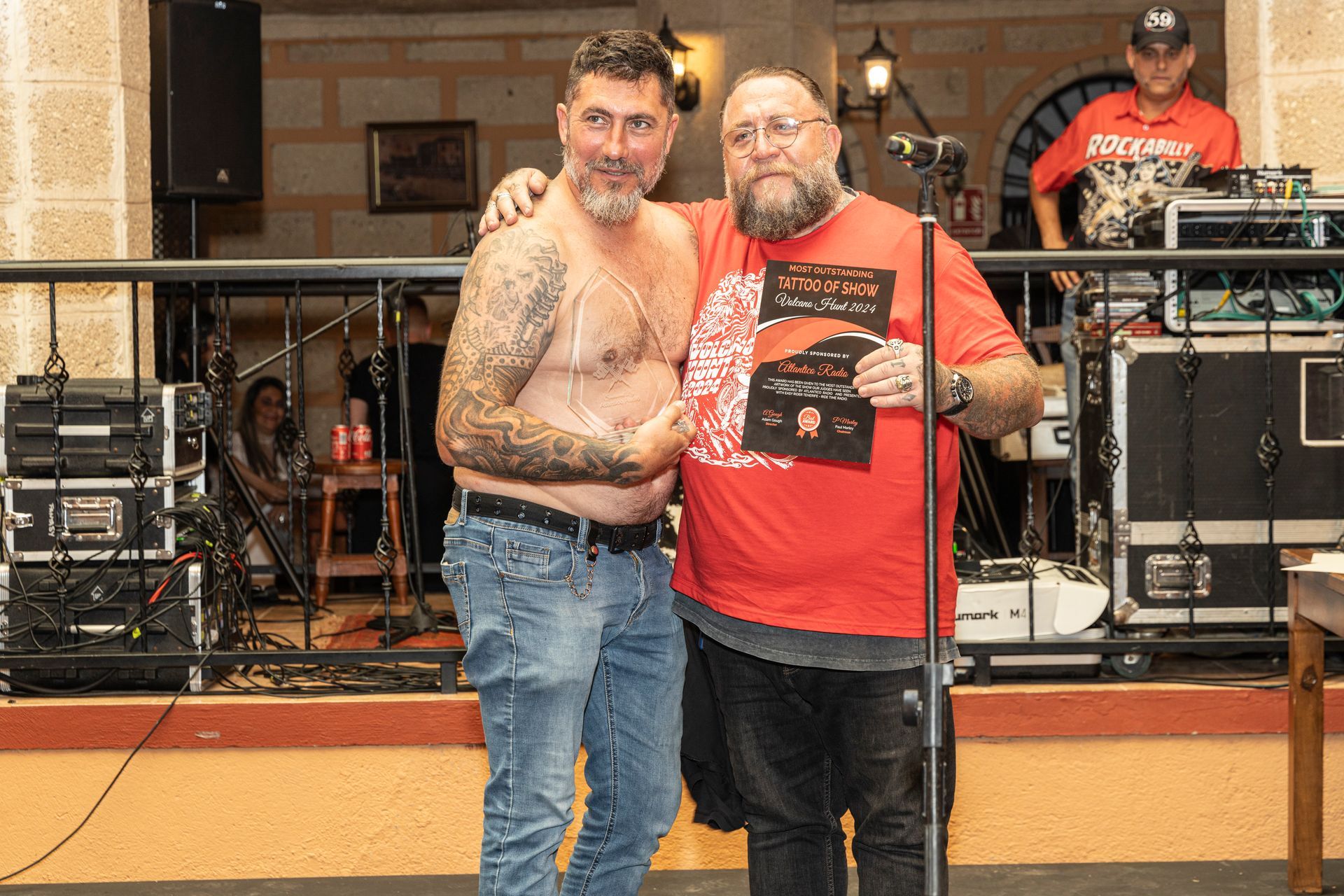 Two shirtless men are standing next to each other in front of a microphone.