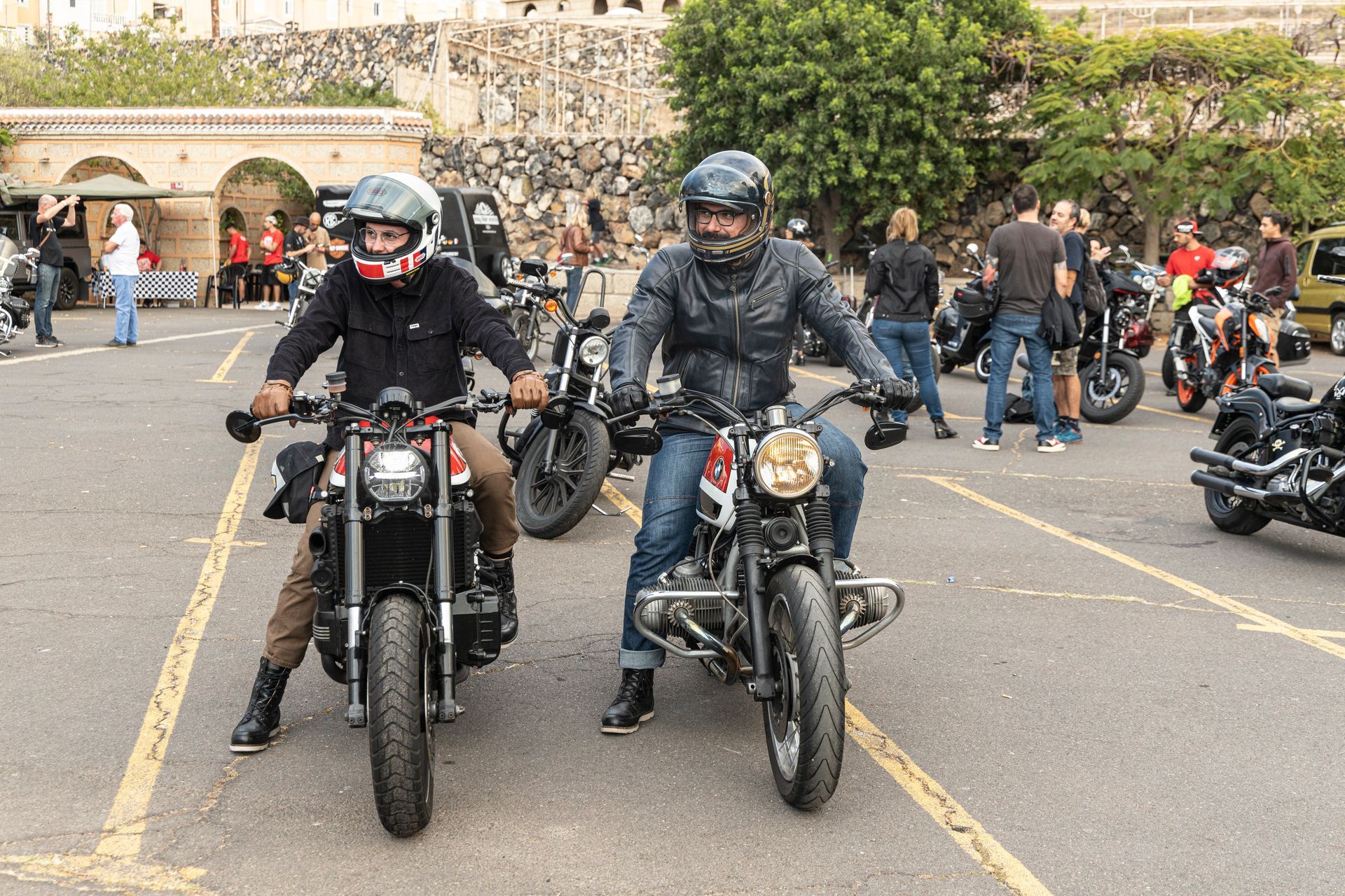 Two men are riding motorcycles in a parking lot.