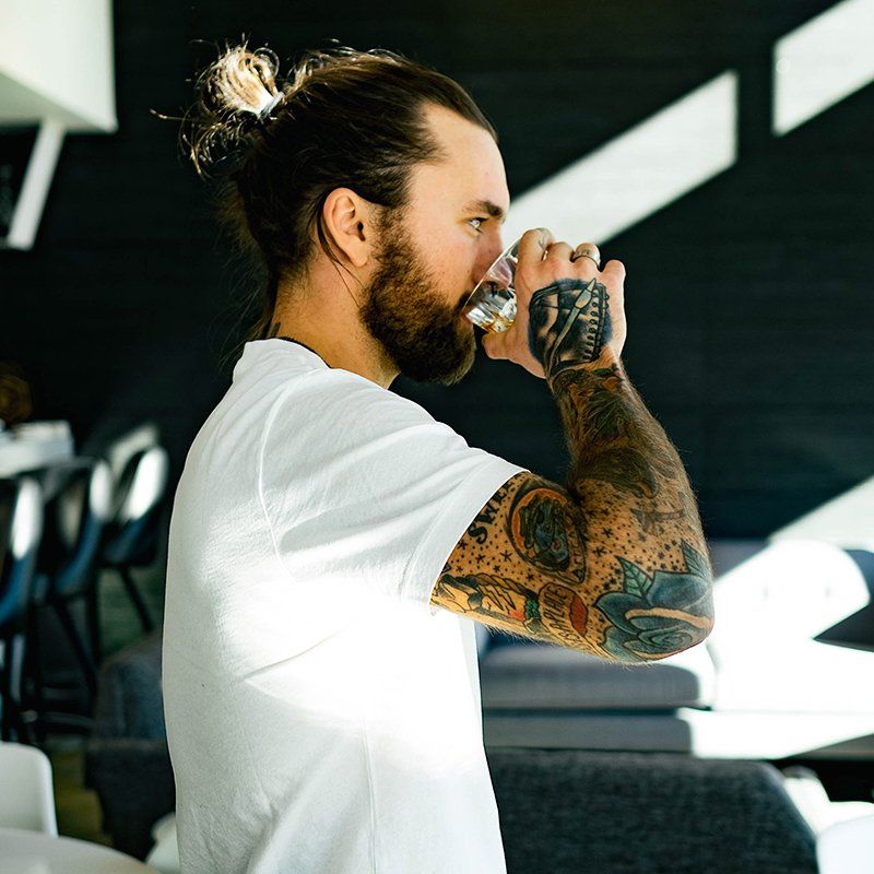 A man with tattoos on his arms is drinking from a glass.