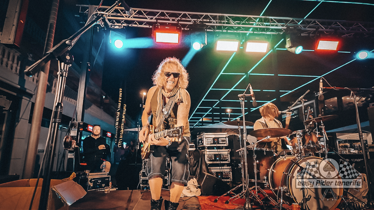 A man with curly hair is playing a guitar on a stage.
