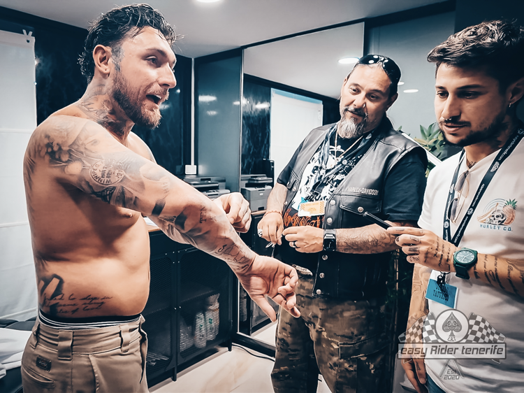 A shirtless man with tattoos is standing next to two other men.