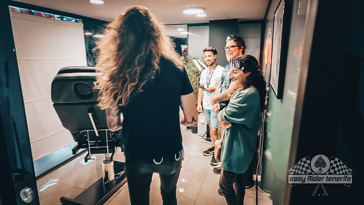 A man with long hair is standing in a room with other people.