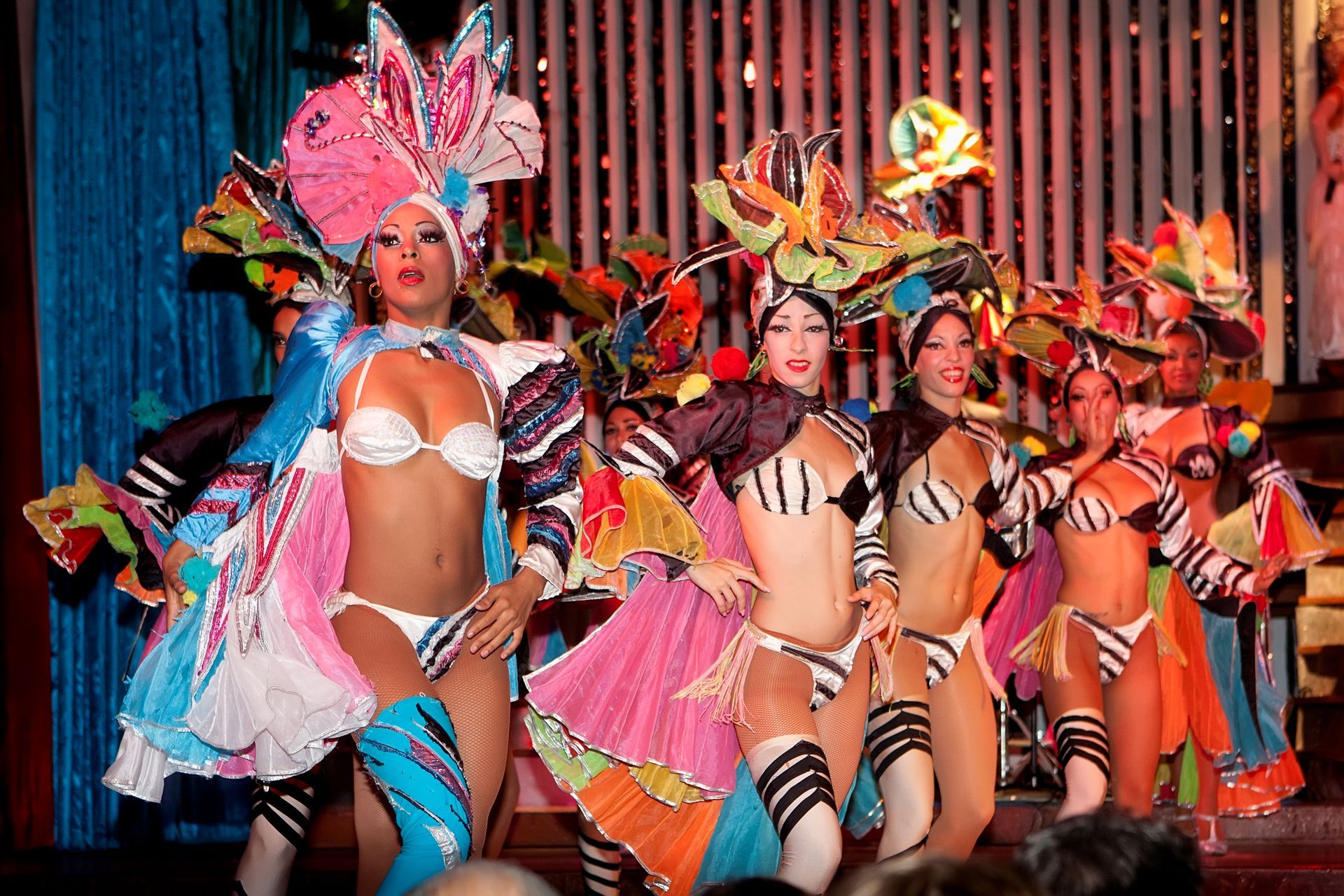Dancers in colorful costumes with headdresses perform on a stage with lights.