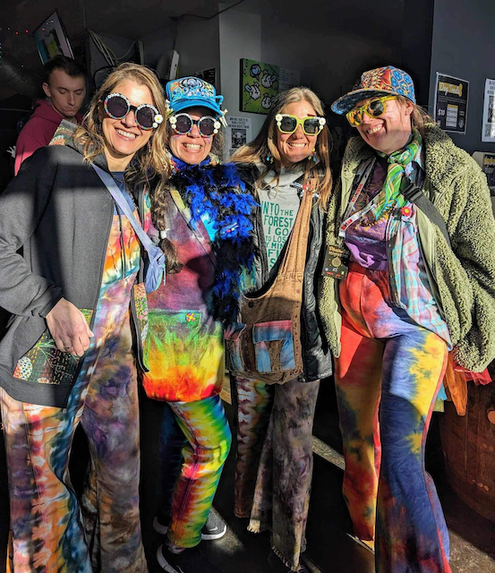 A group of people wearing tie dye clothes are posing for a picture.