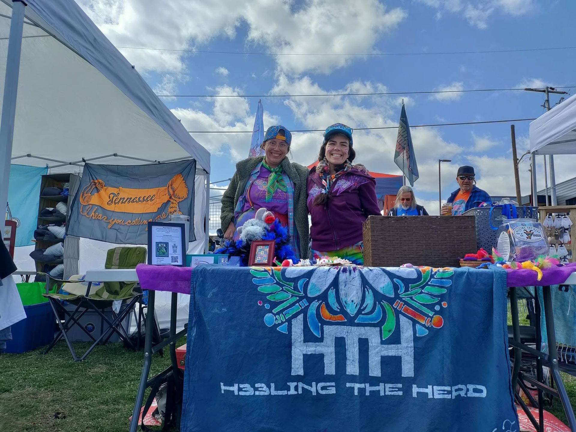Two women are standing behind a table at a festival.