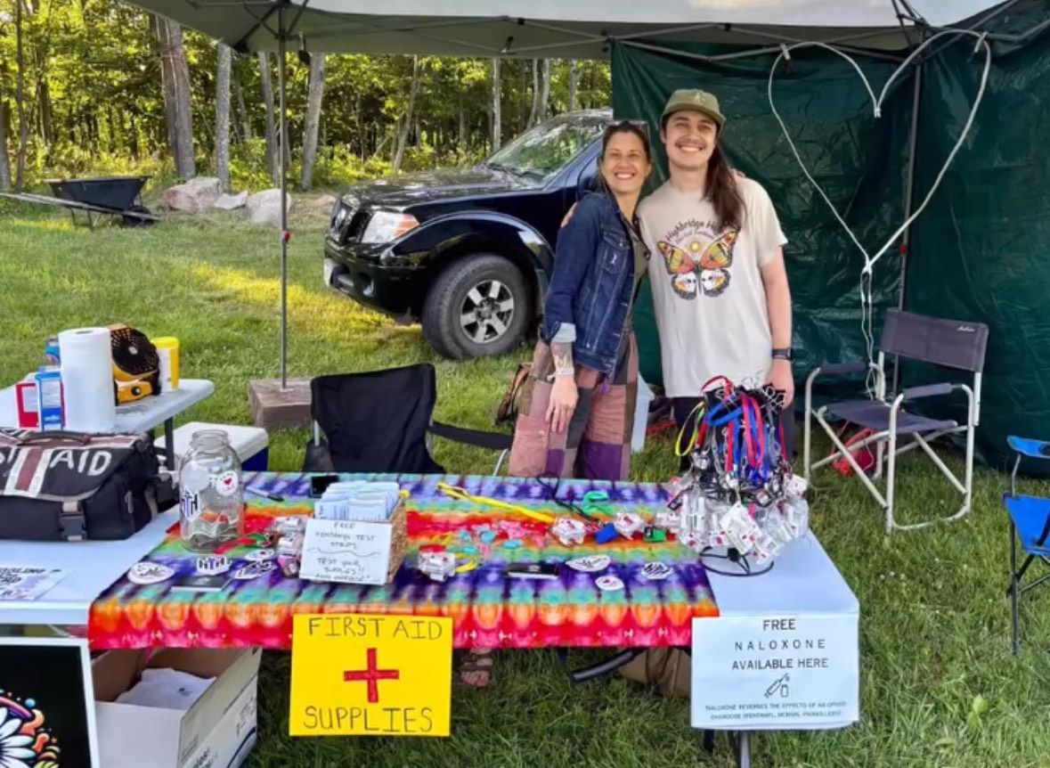 Two women are standing in front of a table with a sign that says `` first aid + cufflets ''.