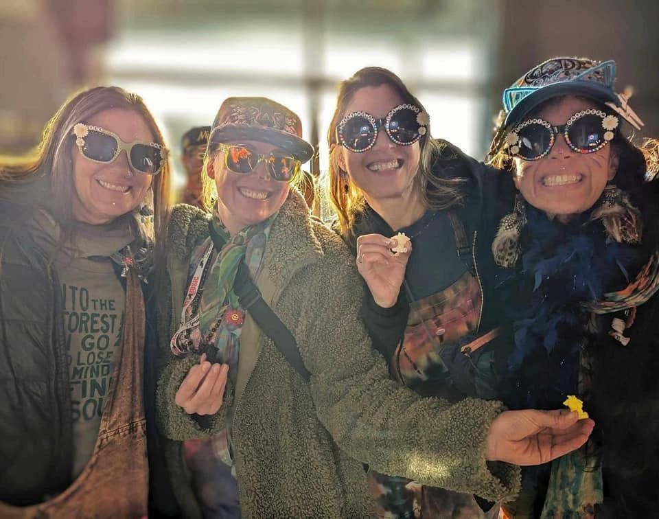 Four women wearing sunglasses and hats are posing for a picture.
