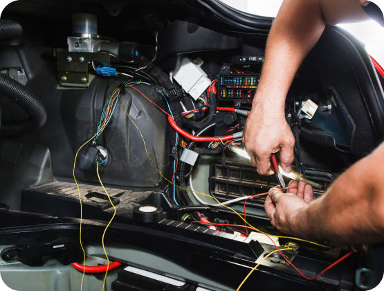 A mechanic working on car wiring in the trunk. The mechanic is holding wires with pliers | Hornick's Diesel & Auto Repair