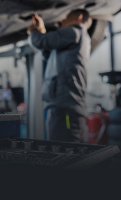 Mechanic working on a car from below in a garage, focusing on underside with tools visible | Hornick's Diesel & Auto Repair