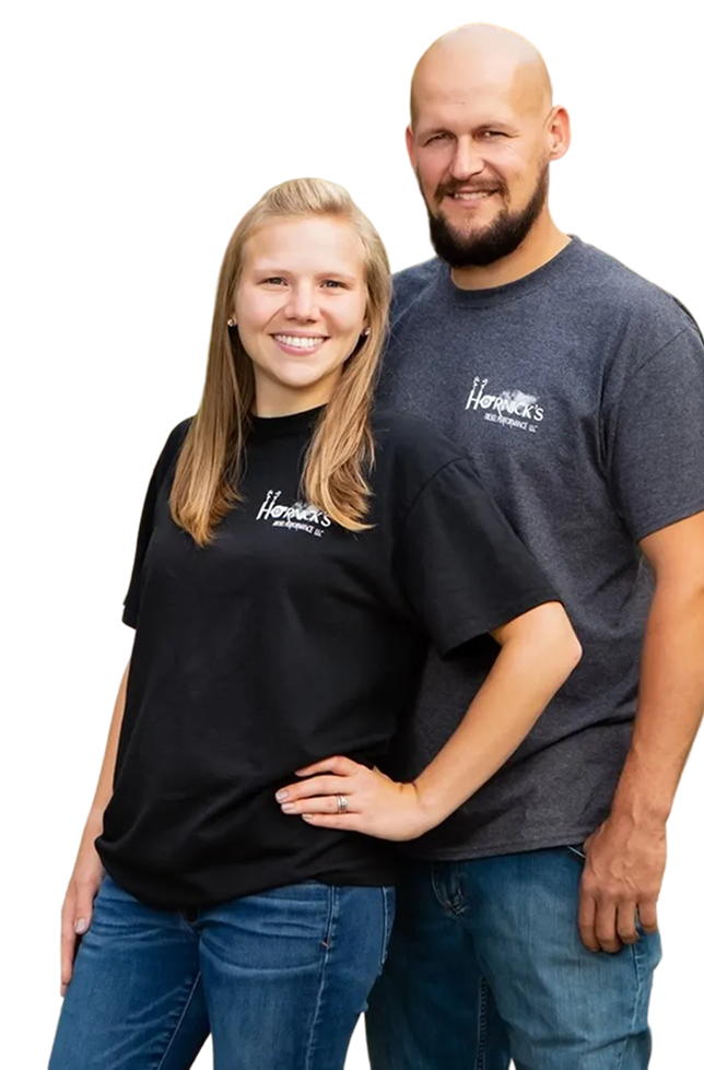 Woman and man wearing matching t-shirts, smiling. Standing together in front of white background | Hornick's Diesel & Auto Repair