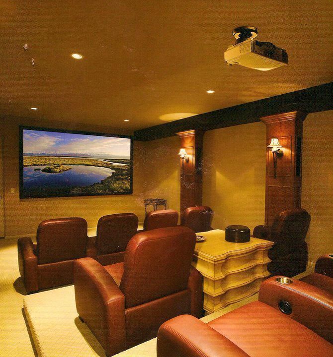Home theater with brown leather recliners facing a large screen, projector on the ceiling, and decorative columns.