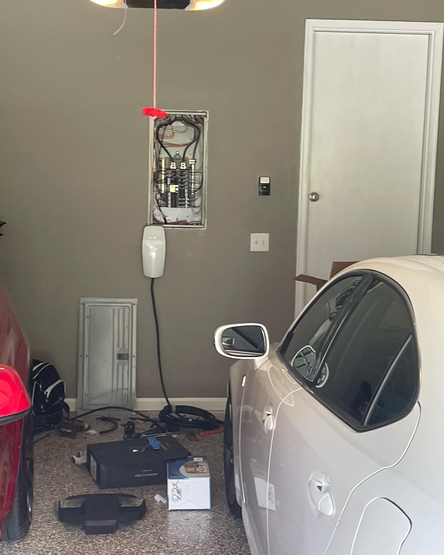 Garage with an electric car, charging station, electrical panel, and tools on the floor.