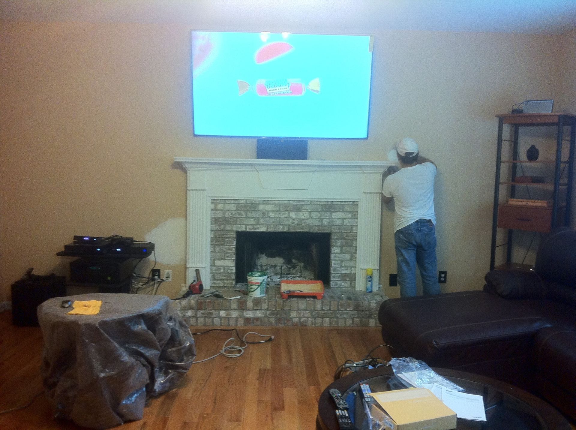 Man installing something over a fireplace, TV mounted above. Living room.