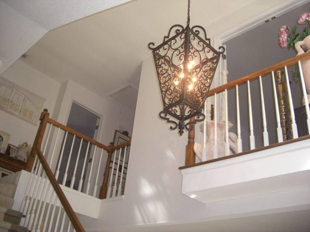 Staircase with ornate chandelier, wooden railing, white walls, leading to a landing with flowers.