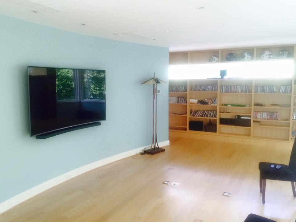A modern room with a mounted TV, wooden floor, and built-in bookshelves; light blue wall.