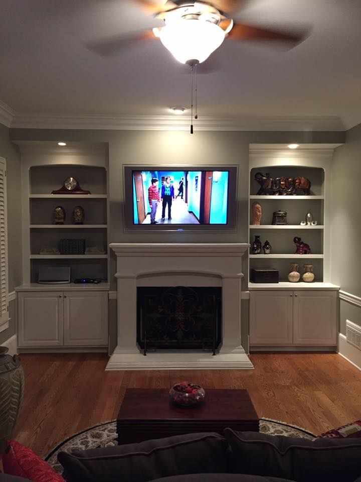Living room with built-in bookshelves flanking a fireplace and TV. Dark wood floor, grey walls, and a ceiling fan.