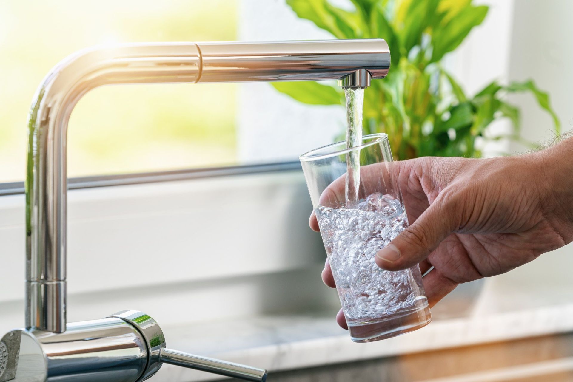 A person is pouring water into a glass from a faucet.