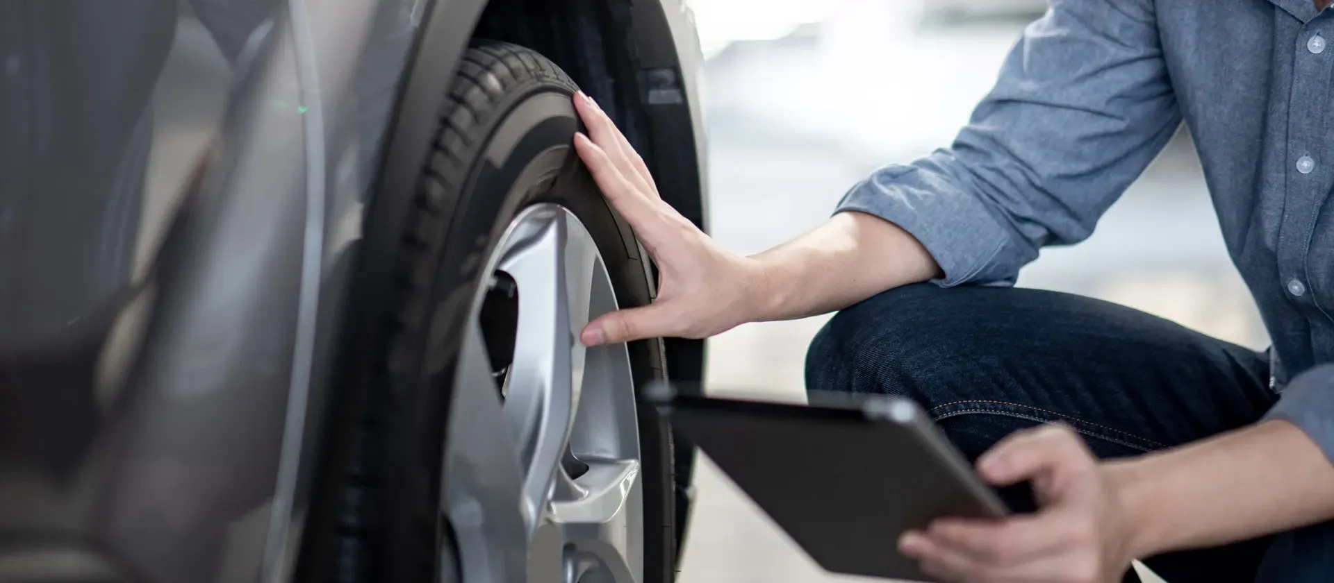 A man is looking at a tire on a car while using a tablet | TLS Motorworks