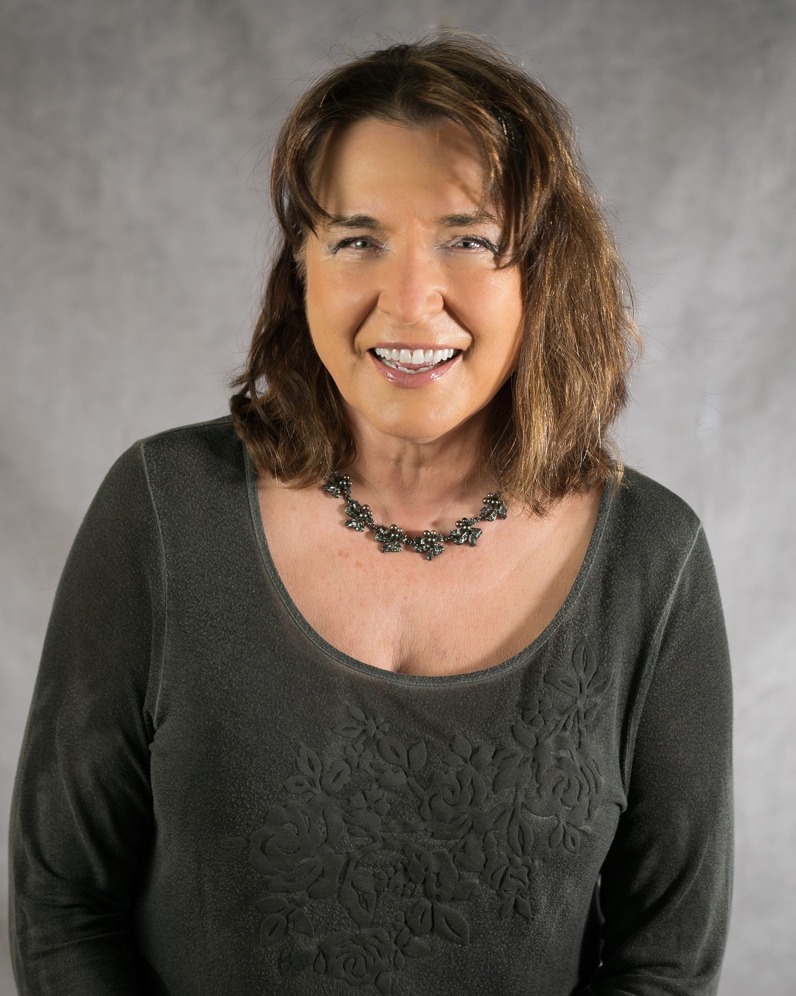 A woman is sitting at a desk with a laptop and a vase of flowers.