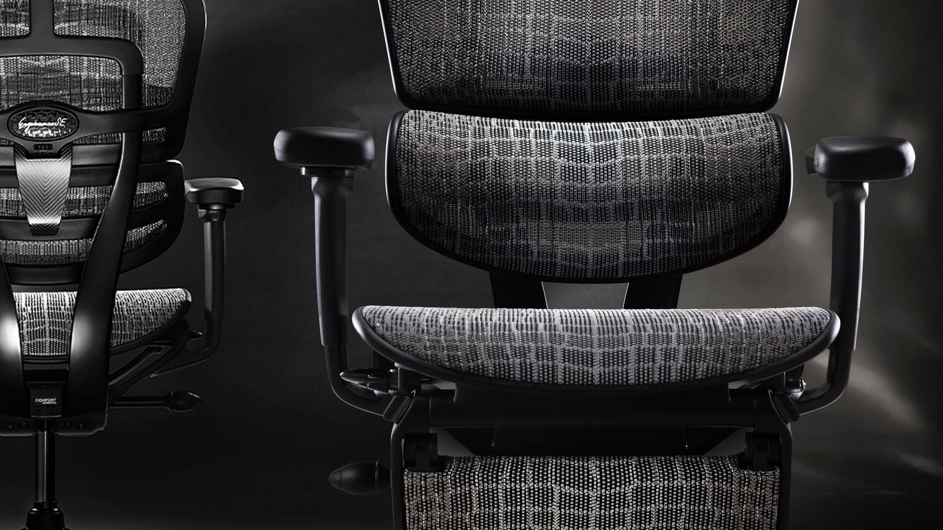 Two Ergohuman carbon chairs against a black background, one facing forward, the other facing back. 