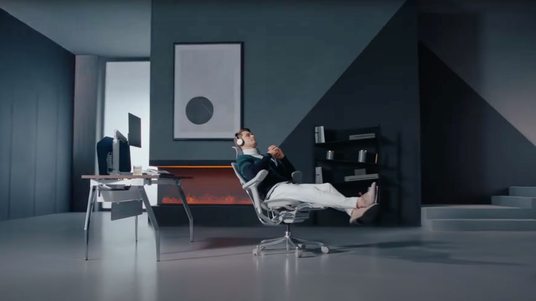 Contemporary grey home office with a stylish man reclining in an Ergohuman mesh office chair. The man is wearing earphones and looks relaxed. The perfect chair for creative work. 