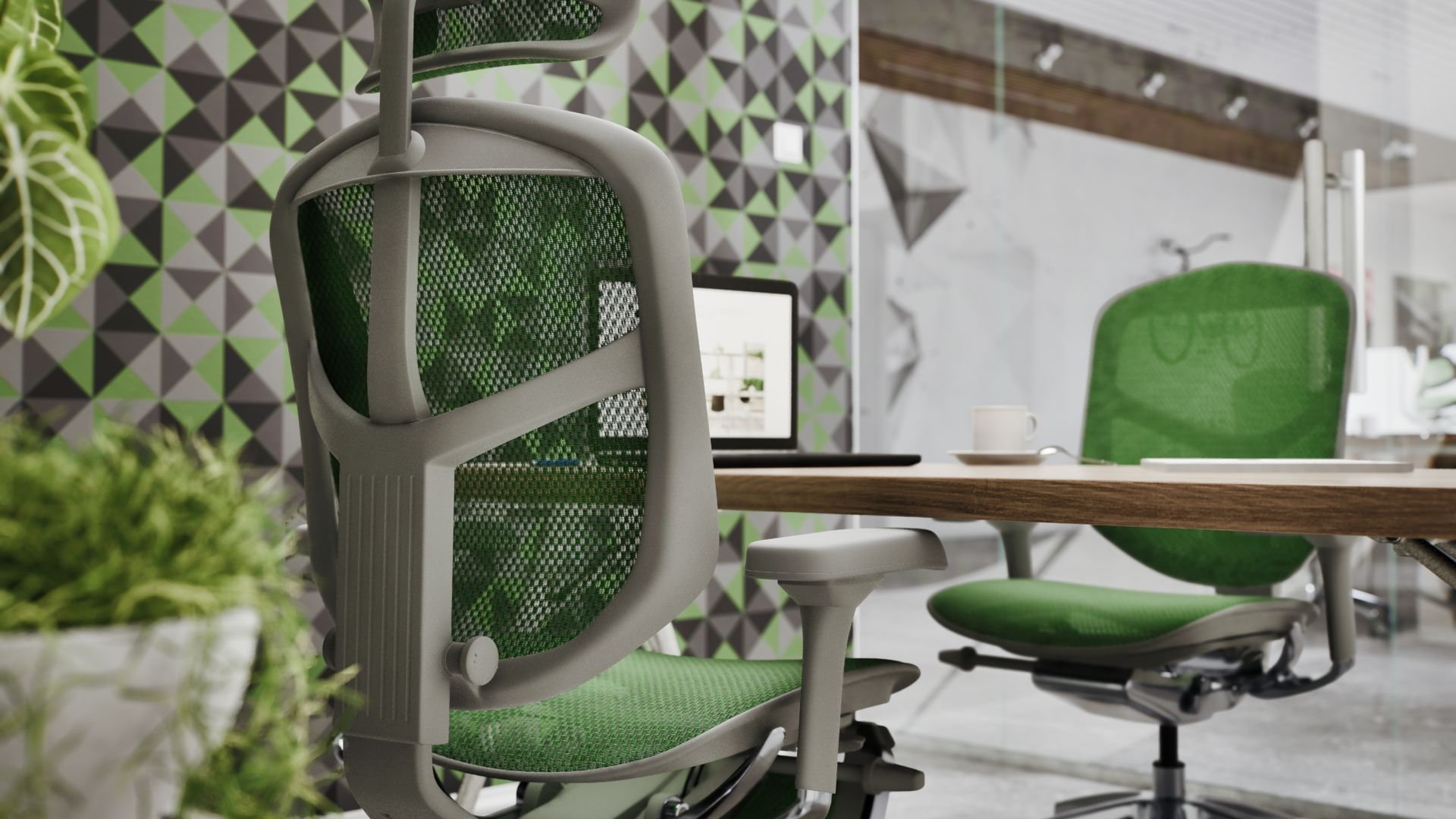 Two green Enjoy Elite with a grey frame at a bench desk in a corporate office with a laptop in the middle of the table and a mug. The walls have geometric patterns in grey, white, black, and green. 