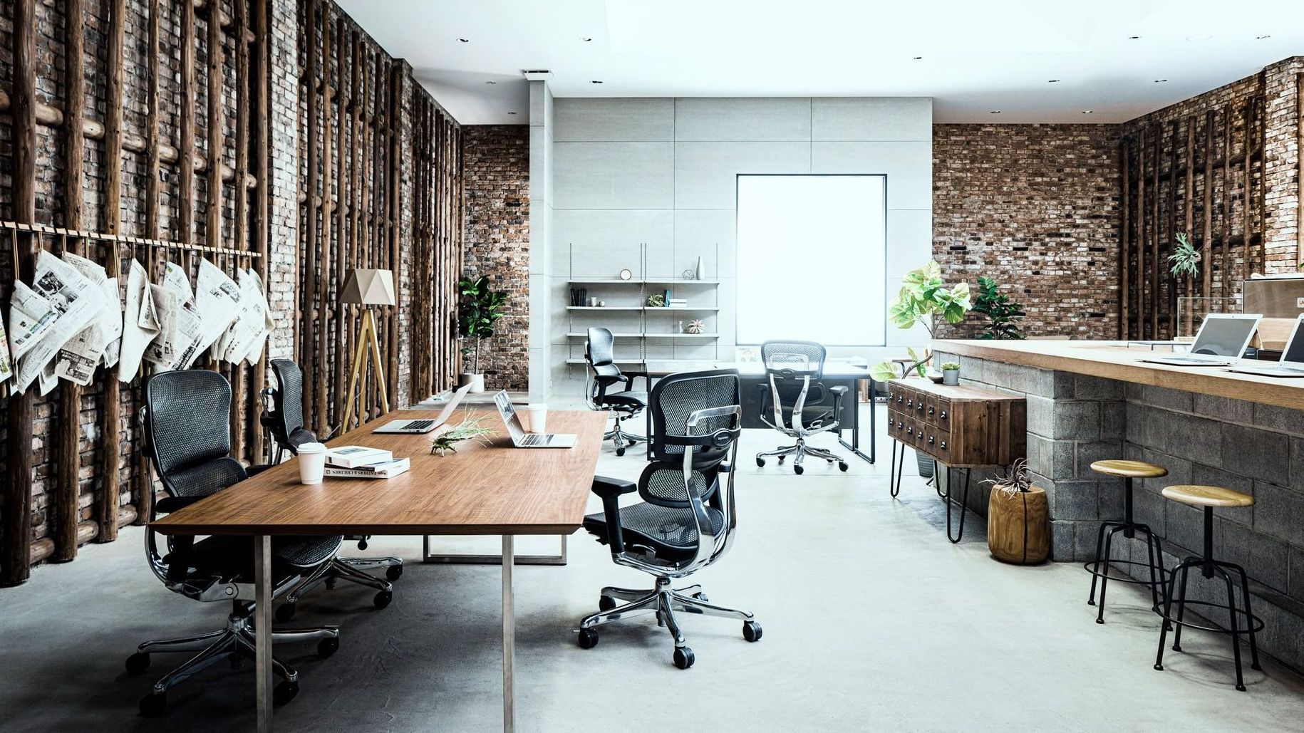 An office space with exposed brick wall and concrete floors. There are a few tables & desks. At each desk are the Ergohuman Elite in black frame with black mesh. 