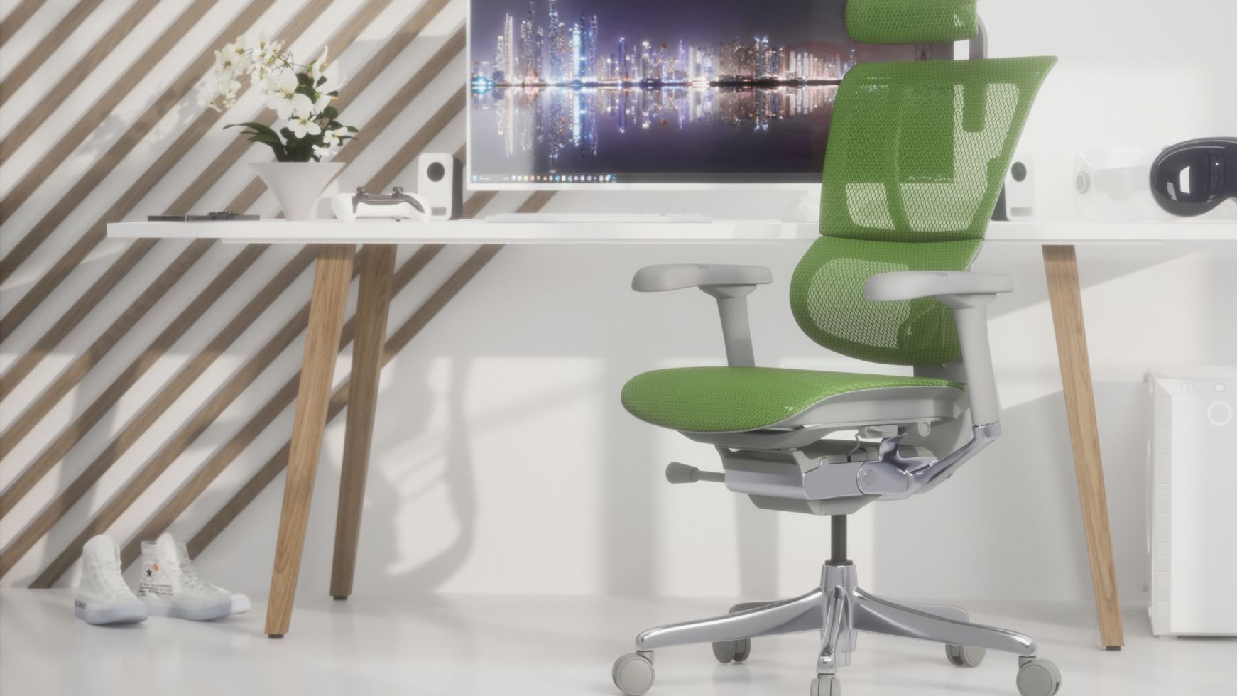 Green Ergohuman office chair in a home office. It's fitted with a grey frame and a headrest. It's at a white desk with wooden legs. On the desk is a large monitor, a pot with flowers, and some gaming equipment for taking a break from work. The office space has white floors and white walls with wooden diagonal beams on the wall. 