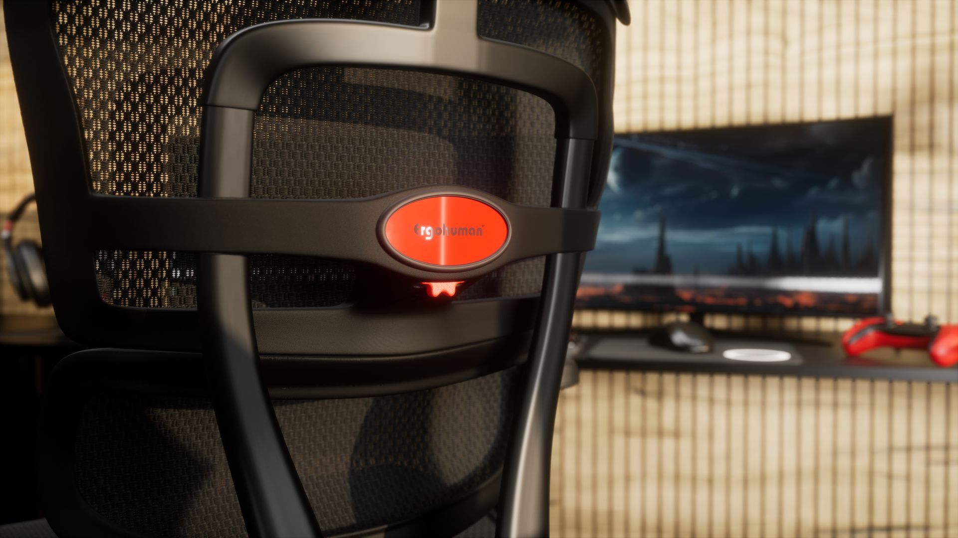 Close up image of the back of an Ergohuman Ultra gaming chair in a black frame with black mesh. This black ergonomic gaming chair is facing a desk. The logo on the back of the chair is a red oval that reads 'Ergohuman' in glossy black letters. 