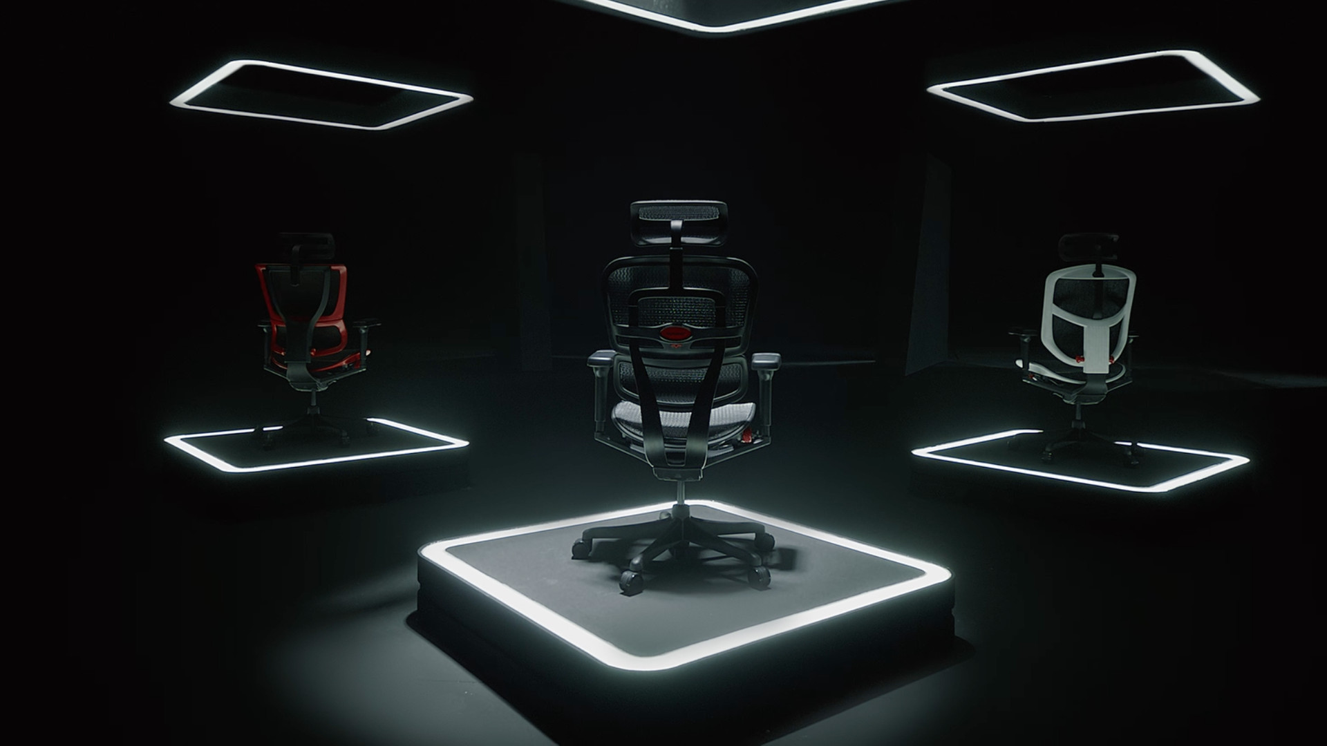 Three Ergohuman gaming chairs, each on a pedestal in 3 different colour options: red, black & white