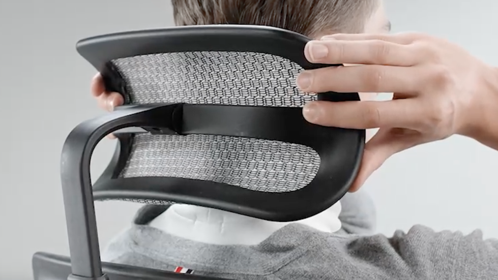 Back view of the Ergohuman headrest. A person is sitting in the chair and we can see their hands on either side of the headrest, making adjustments. 