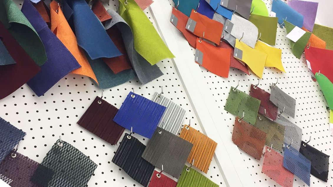 A variety of upholstery option samples. A variety of square samples on a pinboard. They range in colours, including blue, black, orange, green, pink, yellow and more. 