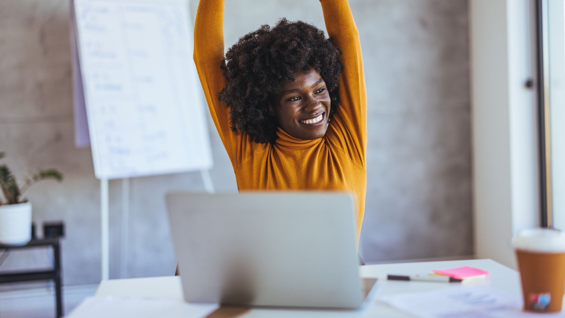 woman in yellow turtleneck stretching upwards while seated at desk