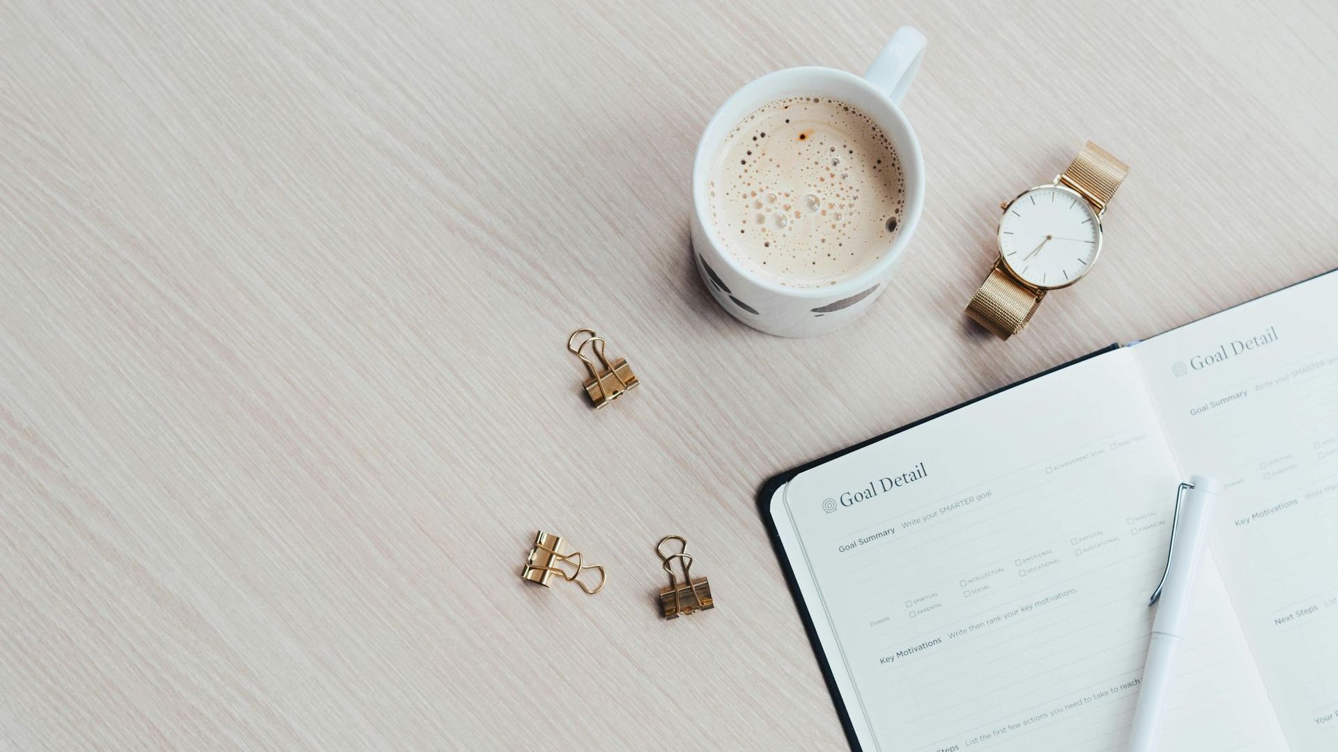 Plan view of a desk with a to-do list notepad, a watch, and pen, some paperclips and a mug of coffee on it,